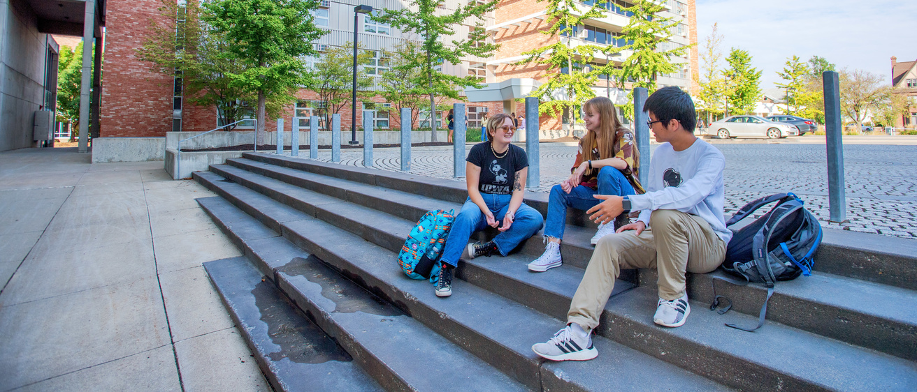 Students sitting on a sidewalk and talking with one another