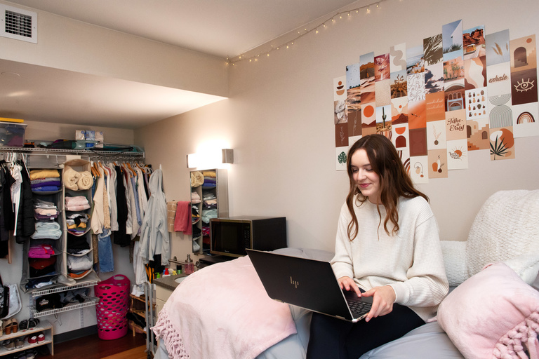 A girl sitting on her bed and typing on a laptop