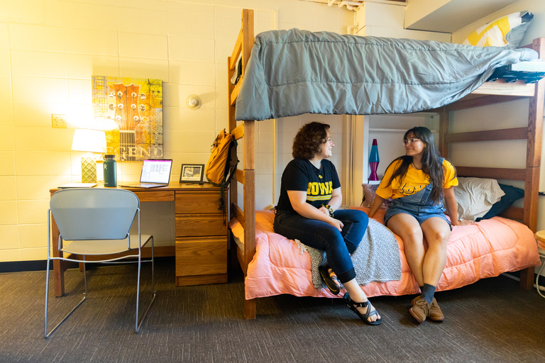 Two student sitting on a bunk bed and talking with one another