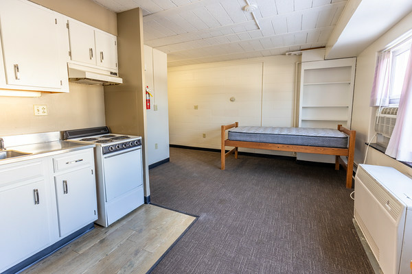 Parklawn studio kitchenette across from the bed and bookshelf, features an oven, stove, full-size refrigerator, cupboards