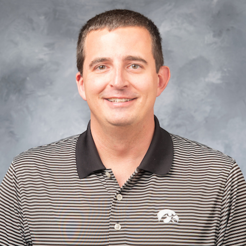 headshot of director Greg Thompson, wearing a black and white striped polo shirt with tiger hawk logo