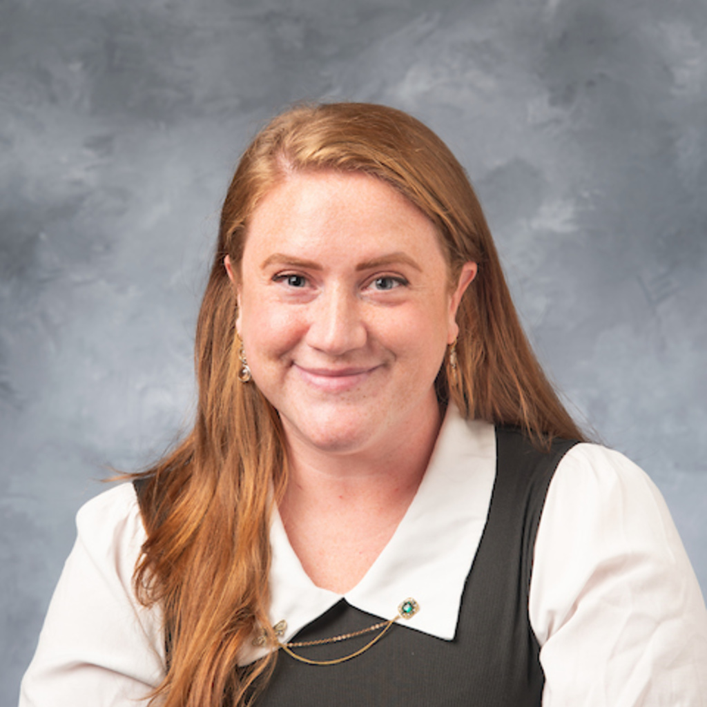 headshot of Susan Presto, redheaded woman in white collared shirt and gray vest