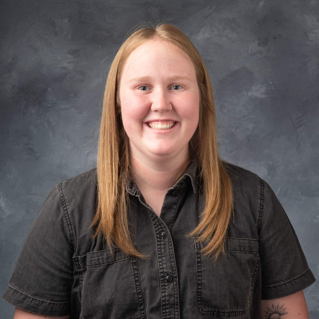headshot of Peyton Ashland, a smiling woman with blond hair and a gray short sleeve button down shirt