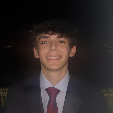 Nighttime head shot of Cole Evans, a young man wearing a navy jacket, blue button up and maroon tie