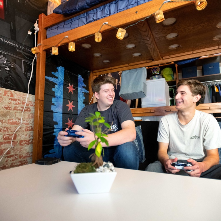 Two male students sitting on a couch playing a video game