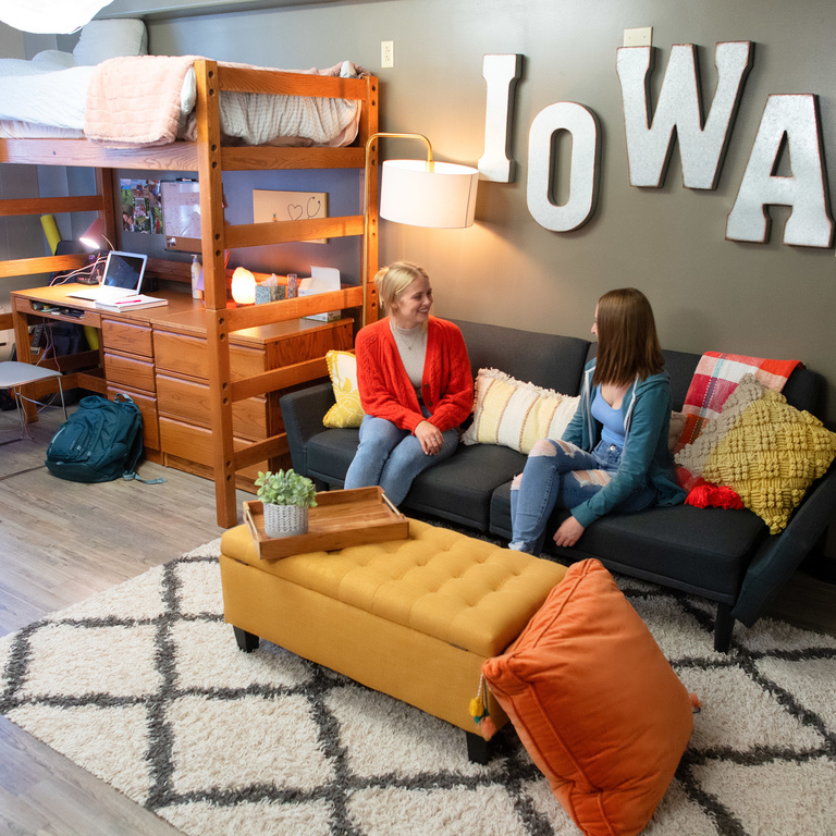 Two students sitting on a couch and talking with Iowa letters in the background