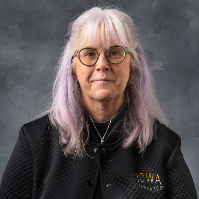 picture of woman with shoulder-length violet-highlighted hair, wearing a black Iowa Hawkeyes shirt and glasses