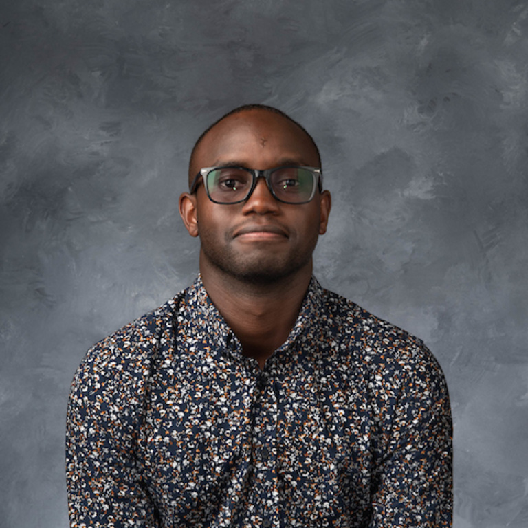 portrait of a Black man wearing eyeglasses and a black, gray, and white patterned button down shirt