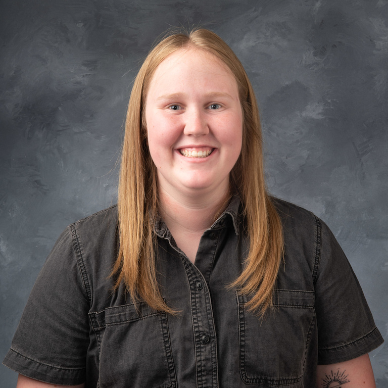 headshot of Peyton Ashland, a smiling woman with blond hair and a gray short sleeve button down shirt