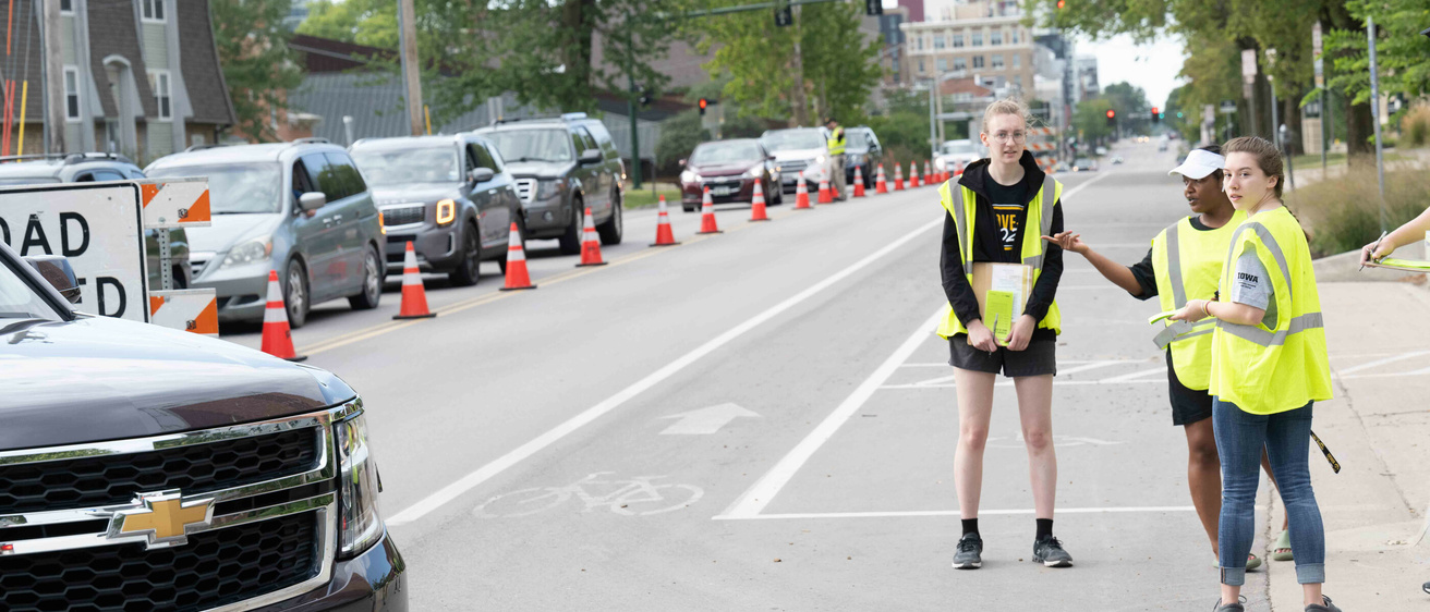 cars line up Clinton Street during Move-in, two student volunteers direct traffic