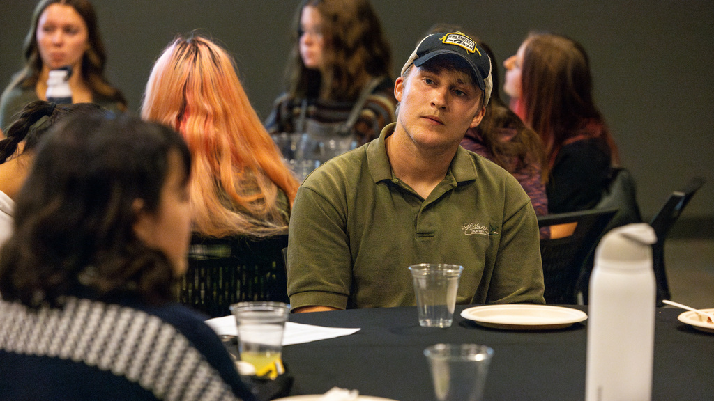 Dinner Dialogue with Leadership and Engagement event, a student wearing a ball cap listens to his table mate discuss conversation techniques