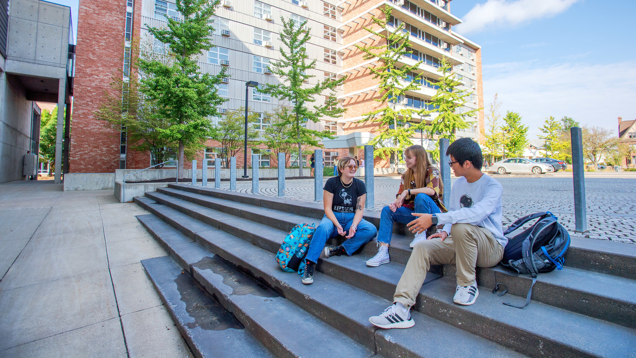 Students sitting on a sidewalk and talking with one another
